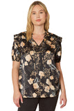 A woman wearing a black floral and ruffle blouse with a V-neck, short puffed sleeves, and ruffle detailing.