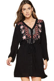 A woman wearing a black embroidered tunic dress with a V-neckline, button down front, and roll tab sleeves.