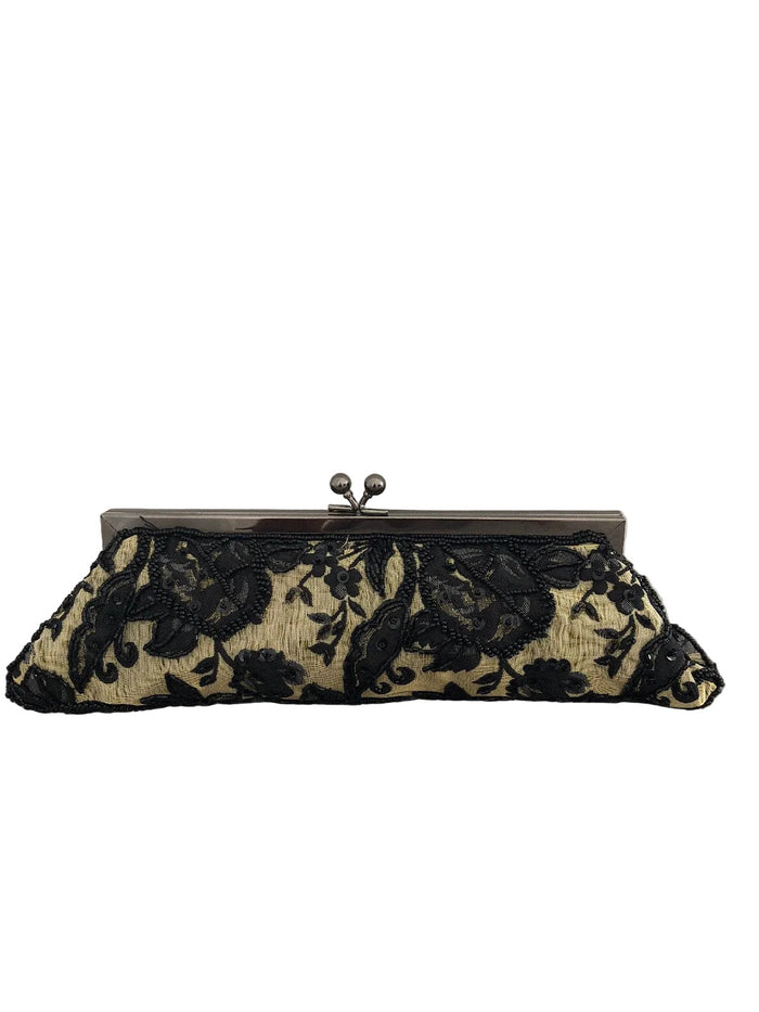 A black floral lace clutch purse with a dark metal kiss-lock clasp, resting on a gray carpet against a white wall.
