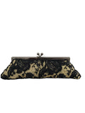 A black floral lace clutch purse with a dark metal kiss-lock clasp, resting on a gray carpet against a white wall.