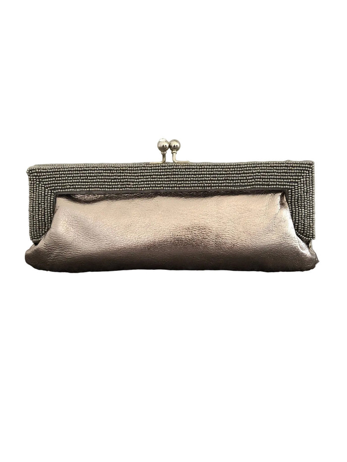 A metallic champagne clutch purse with a textured beaded frame and silver-tone kiss-lock clasp, resting on a gray carpet against a plain wall.