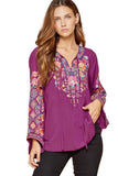 Woman wearing a purple embroidered blouse against a beige background