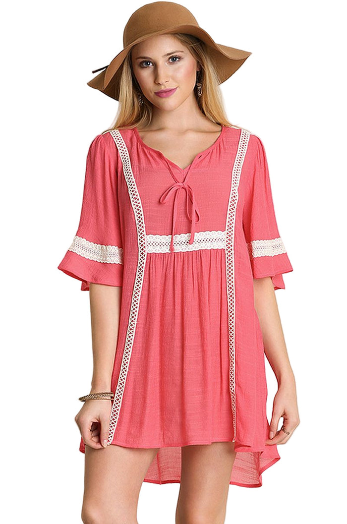 Woman wearing a coral dress with white lace trim and a brown hat on a beige background