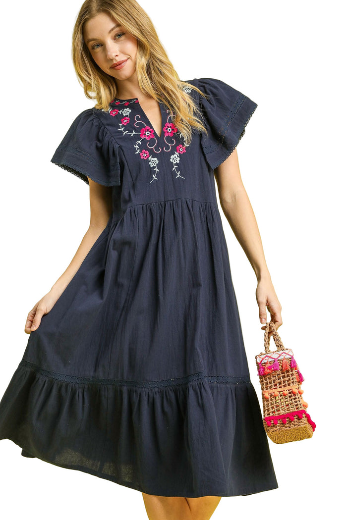 Woman wearing a navy dress with floral embroidery against a yellow background