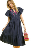 Woman wearing a navy dress with floral embroidery against a yellow background
