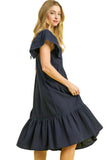 Woman wearing a navy dress with ruffled sleeves and hem on a yellow background, featuring Umgee branding.