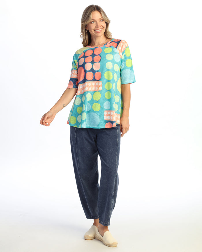 Woman wearing a colorful polka dot shirt and blue jeans on a white background