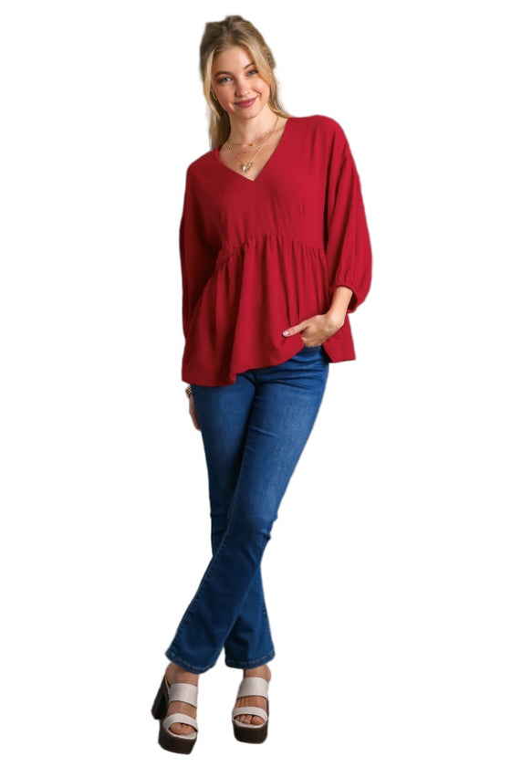 Woman wearing a red blouse and blue jeans against a gray background