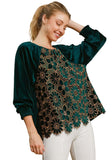 Woman wearing a hunter green blouse with intricate lace detailing on a beige background