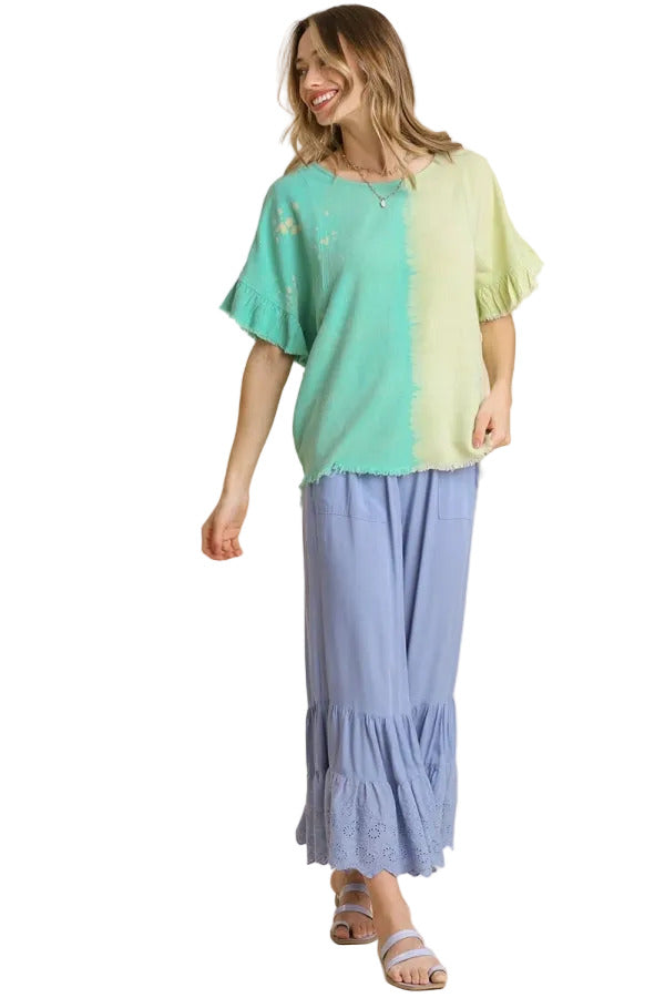 A woman modeling a two-tone split-color top in mint green and pale yellow-green, paired with light blue tiered maxi pants, against a solid beige background.