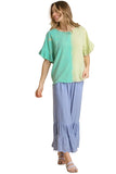 A woman modeling a two-tone split-color top in mint green and pale yellow-green, paired with light blue tiered maxi pants, against a solid beige background.