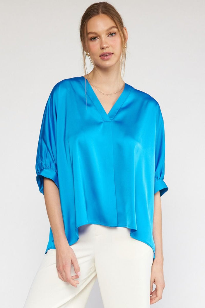 Woman wearing a blue blouse and white pants on a plain background